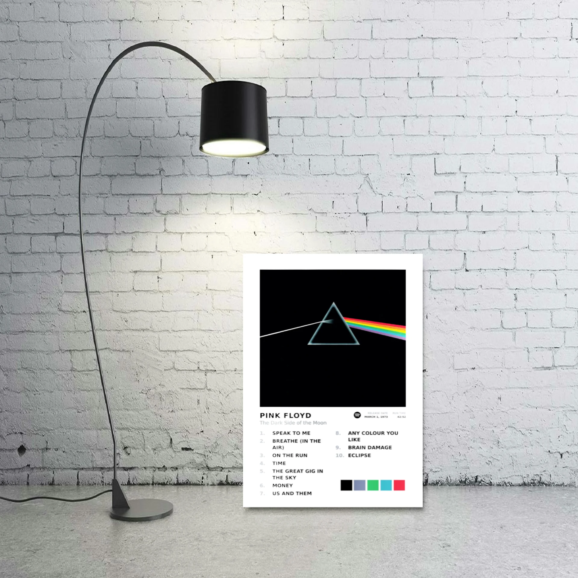 Pink Floyd album art metal print leaning against a white brick wall beside an arc lamp