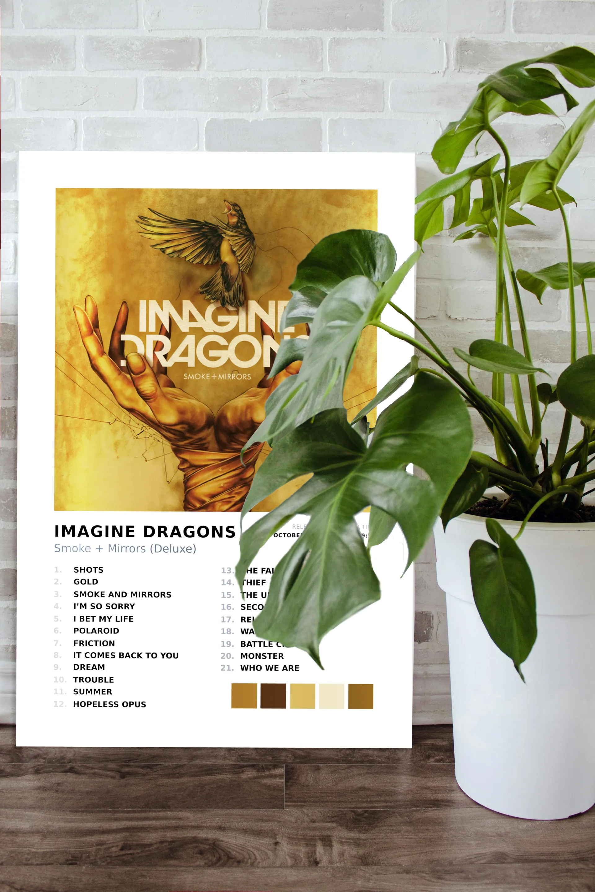 Imagine Dragons album metal print propped against a white brick wall with a monstera plant